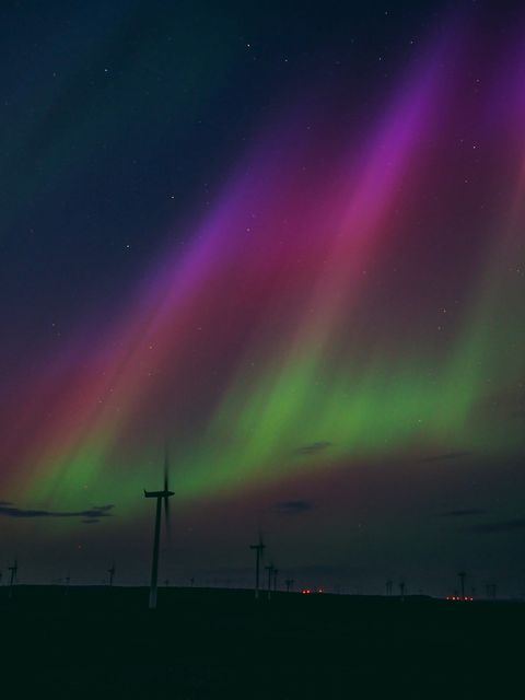 silhouette of a wind turbine against aurora sky