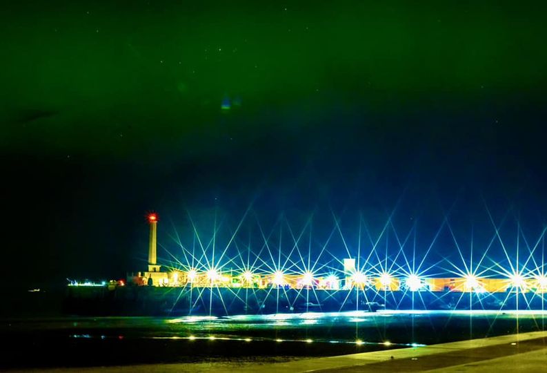 Photo of green aurora skies with starbirsts on the pier in the foreground